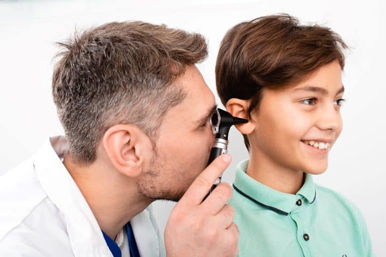 An audiologist looks inside the inner ear of a pediatric patient using a medical tool.